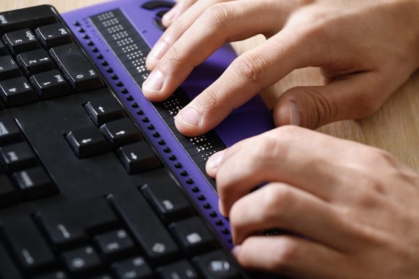 A pair of hands using computer with braille computer display and a computer keyboard.